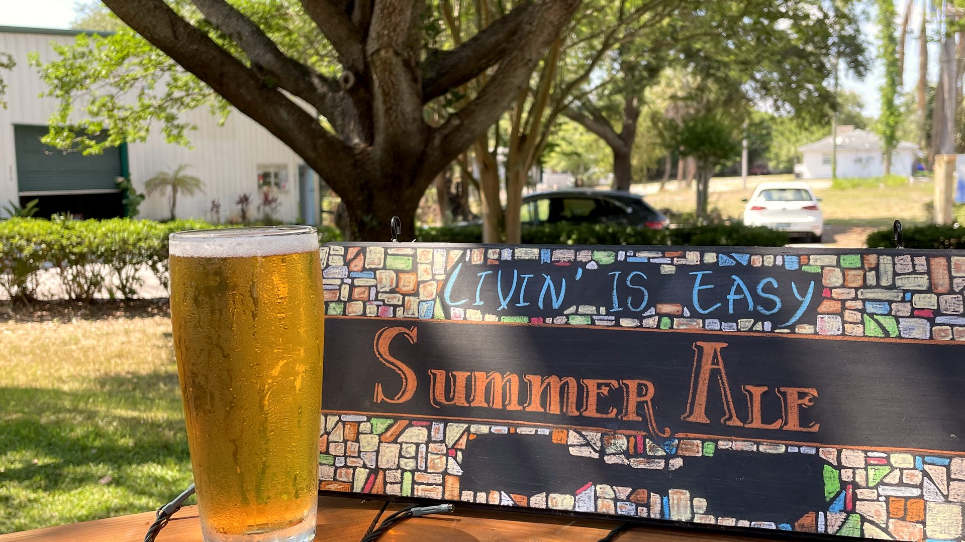 Pint of Livin’ Is Easy Summer Ale next to its hand-painted sign on the deck rail