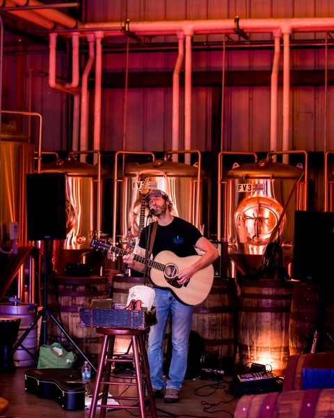 A guitarist performing in the brewhouse in front of the tanks