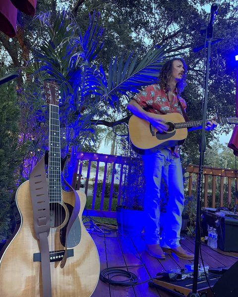 A guitarist performing on the deck stage under blue lights