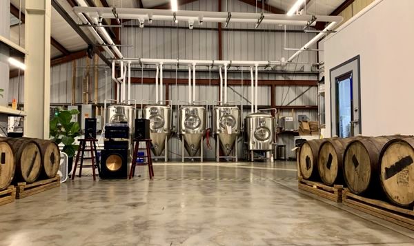 The Brighter Days brewhouse: stainless fermentation tanks and wooden barrels, with a band's speakers and amp set up on the floor