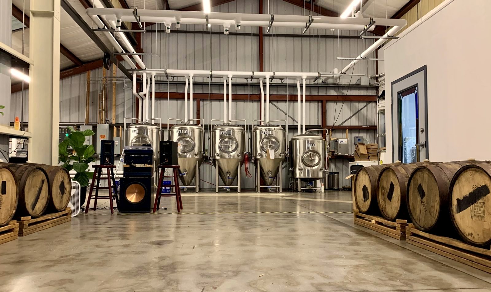 The Brighter Days brewhouse: stainless fermentation tanks and wooden barrels, with a band's speakers and amp set up on the floor