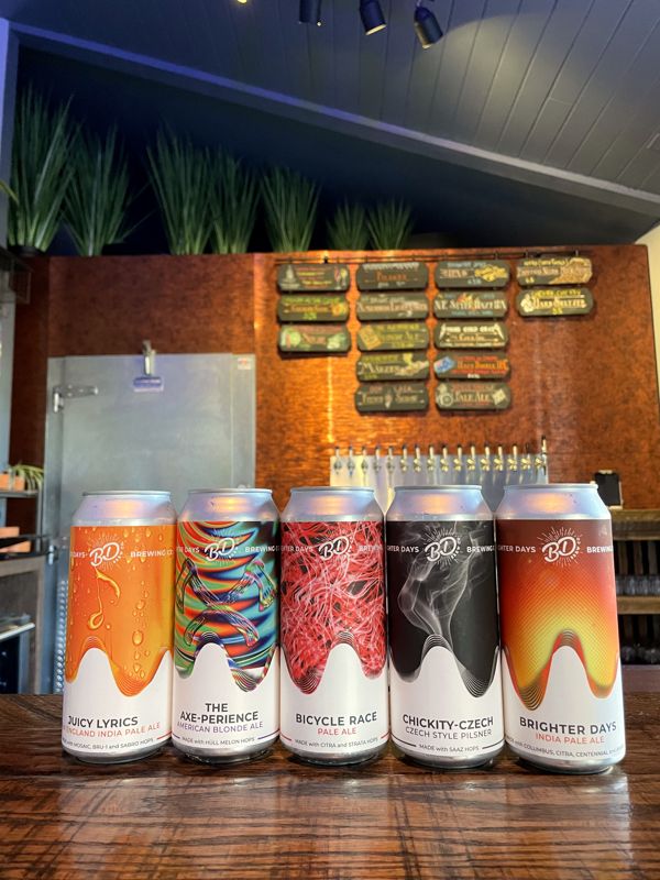 Five Brighter Days cans with colorful labels lined up on the bar in front of the tap wall