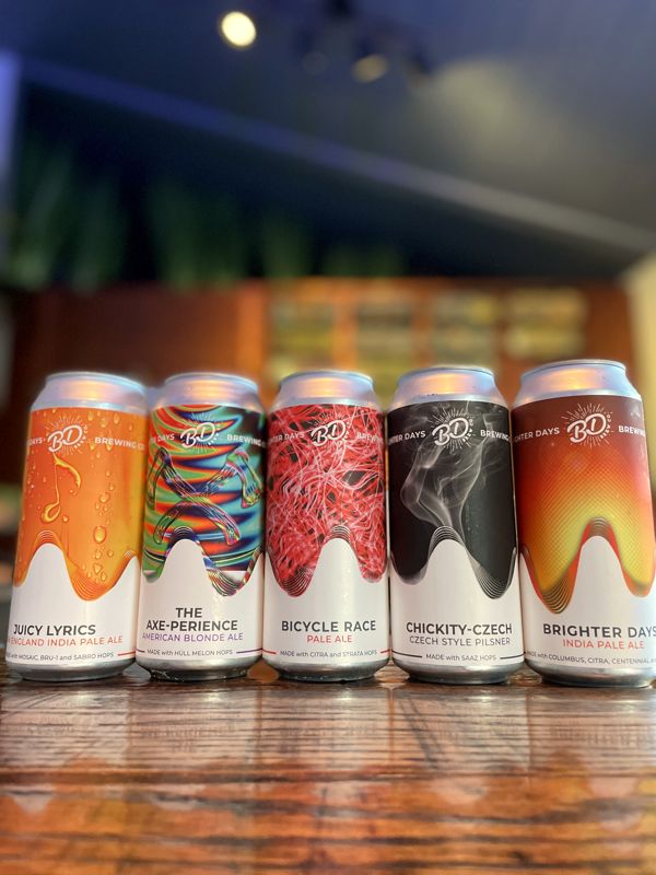 Close row of five Brighter Days cans with colorful labels on a wooden bar