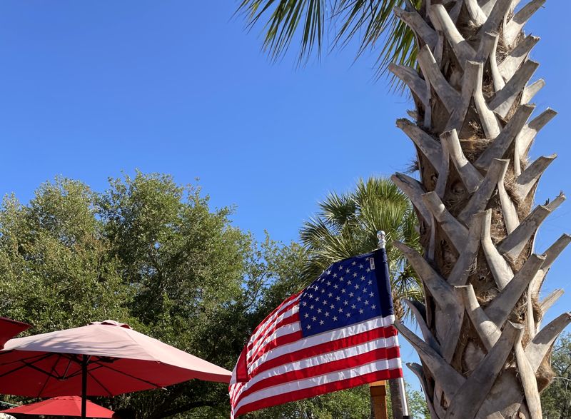 Red umbrellas, an American flag and a palm tree over the patio on a sunny day