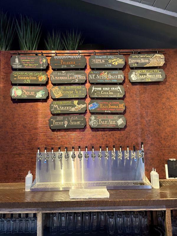 Brick wall of hanging beer menu signs above a row of chrome tap faucets